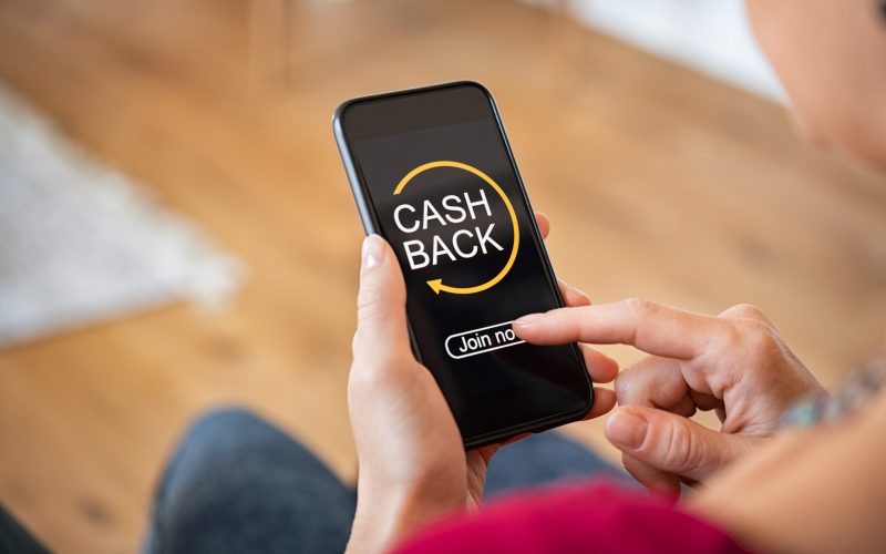 Woman taking benefit of cashback using smart phone, shopping and money refund concept. Woman hand holding smartphone with button to get started the cashback. Close up of girl holding mobile phone while clicking on join now option in app.